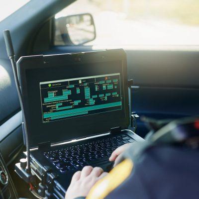 Cropped shot of an unrecognizable male police officer using his laptop while out on patrol